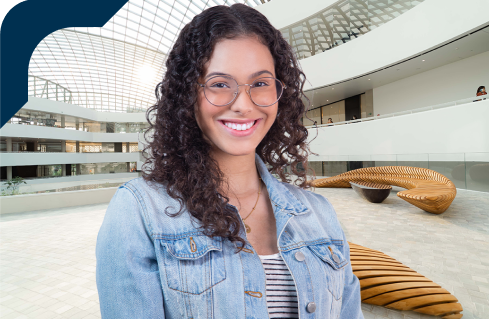 Estudante universitária sorrindo, usando óculos e jaqueta jeans, na Unidade de Ensino Einstein.