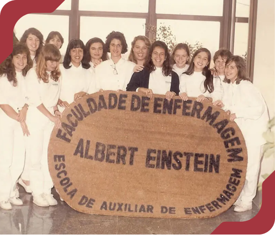 Foto histórica de alunas do curso de Enfermagem do Einstein segurando um banner da 'Faculdade de Enfermagem Albert Einstein'.