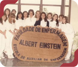 Foto histórica de alunas do curso de Enfermagem do Einstein segurando um banner da 'Faculdade de Enfermagem Albert Einstein'.